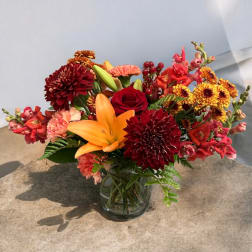 Mixed bouquet with red roses, orange lilies, and burgundy mums in a glass vase