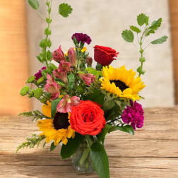 Mixed bouquet with sunflowers, red roses, and pink alstroemeria in a glass vase
