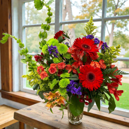 Bright mixed bouquet in a clear glass vase with red gerbera daisies and orange roses