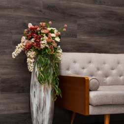 Tall floral arrangement in a silver vase beside a beige sofa