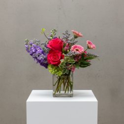 Mixed bouquet in a clear glass vase with pink roses and purple blooms