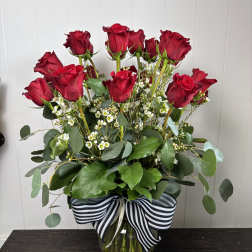 Red roses arranged in a clear glass vase with a striped ribbon.