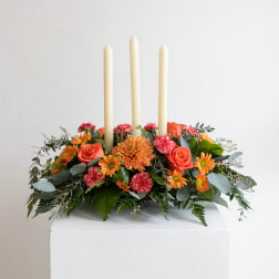 Orange and pink floral centerpiece with three ivory taper candles