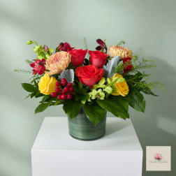 Mixed bouquet of red, yellow, and peach flowers in a green vase