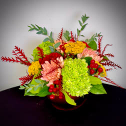 Colorful floral arrangement in a low red vase with pink, green, and yellow blooms