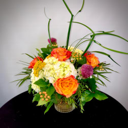 Orange roses and white hydrangeas in a glass vase with tall grass accents