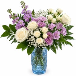 White roses and lavender flowers arranged in a blue glass vase