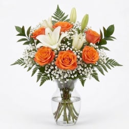 Orange roses and white lilies in a clear glass vase