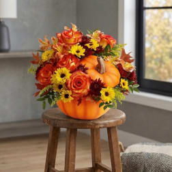Orange pumpkin centerpiece with roses and daisies on a stool