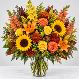 Bright mixed bouquet with sunflowers, roses, lilies, and chrysanthemums in a glass vase