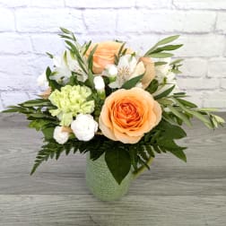 Peach roses and white flowers arranged in a green mug vase