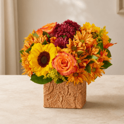 Mixed bouquet of sunflowers, roses, and mums in a carved square vase