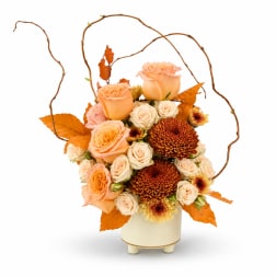 Peach roses and cream spray roses in a cream vase with autumn leaves