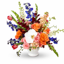 Colorful mixed bouquet in a white vase with roses and orchids