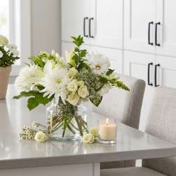 White floral arrangement in a clear glass vase on a table beside a candle