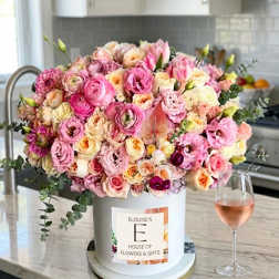 Large pink and cream floral arrangement in a white hat box beside a wine glass