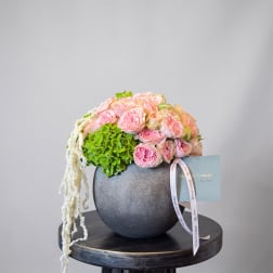 Pink roses and green hydrangea in a dark round vase with trailing white flowers