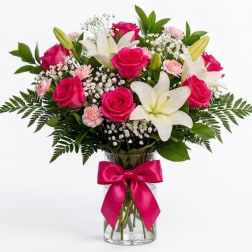 Pink roses and white lilies in a glass vase with a pink ribbon