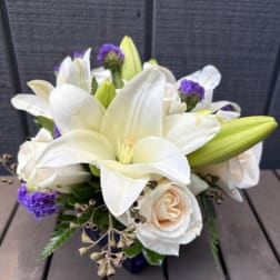 White lilies and cream roses arranged with purple accents in a vase