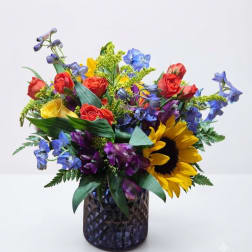 Colorful bouquet with roses, sunflowers, and blue flowers in a dark glass vase