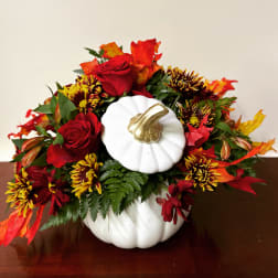 Fall floral arrangement in a white pumpkin container with red roses and mums