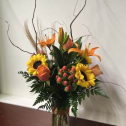 Orange lilies and sunflowers arranged in a clear glass vase