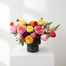 Mixed pink, yellow, and orange roses in a dark glass vase