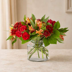 Red roses and orange flowers arranged in a clear glass vase