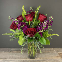 Bouquet of red roses and purple flowers in a clear glass vase
