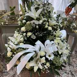 Tall white and cream lily and rose arrangement in a wicker basket with white ribbon bows