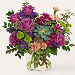 Purple roses and mixed flowers arranged in a clear glass vase with a succulent center.