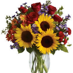 Bouquet of sunflowers, red roses, and purple daisies in a clear glass vase