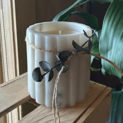 White ribbed candle wrapped with twine and dark leaf sprigs