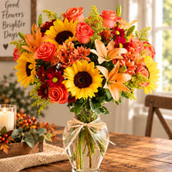 Bright mixed bouquet with sunflowers, roses, lilies, and daisies in a glass vase