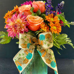 Colorful bouquet of roses, dahlias, and daisies in a green vase with a pumpkin ribbon