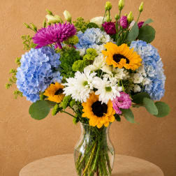 Mixed bouquet of sunflowers, hydrangeas, and daisies in a clear glass vase
