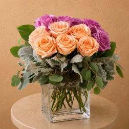 Peach and purple roses in a clear square vase