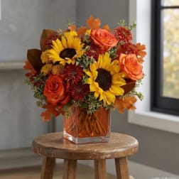 Autumn bouquet with sunflowers and orange roses in a square glass vase