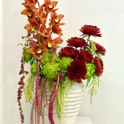 Orange orchids and burgundy mums in a white vase