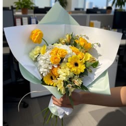 Handheld bouquet of yellow and white flowers wrapped in pale paper