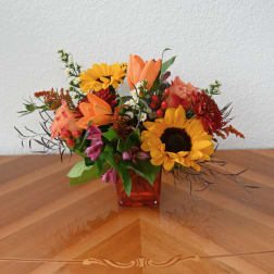 Mixed bouquet in a red glass vase with sunflowers, lilies, and orange blooms