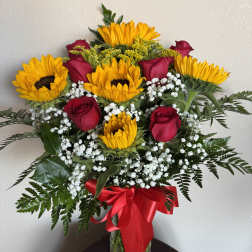 Sunflowers and red roses in a glass vase with a red ribbon