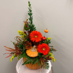 Autumn floral arrangement in a pumpkin container with orange gerberas and yellow accents