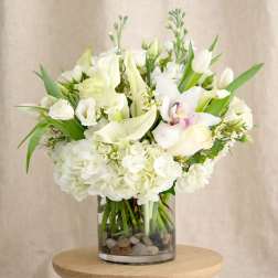 White floral arrangement in a clear glass vase with stones
