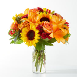 Bouquet of sunflowers, orange lilies, and roses in a clear glass vase
