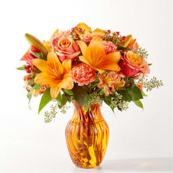 Orange lilies and roses arranged in an amber glass vase
