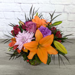 Orange lilies and purple flowers in a low vase arrangement