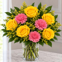 Yellow roses and pink carnations in a clear glass vase