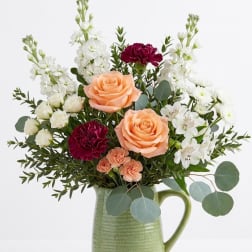 Peach roses and white flowers arranged in a green ceramic pitcher
