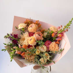 Mixed bouquet of peach, pink, and cream flowers wrapped in pastel paper